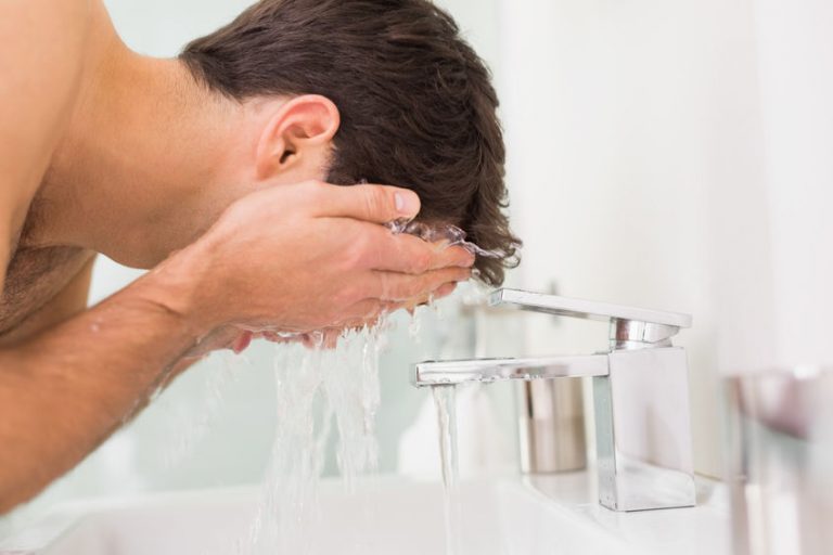 Side view of a shirtless young man washing face in the bathroom